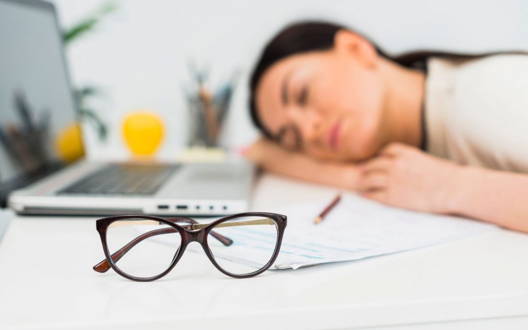 woman with glasses asleep on an office table beside laptop